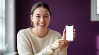 Happy young Asian woman showing blank smartphone screen with thumbs up gesture in modern purple interior for mobile app presentation.