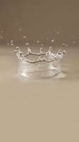 Clear water crown splash with droplets frozen in motion on neutral beige background. High-speed photography captures liquid dynamics for science and nature concepts.