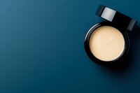 Open black luxury cosmetic jar with creamy beige face cream on deep blue background, top view with copy space for beauty and skincare brands.