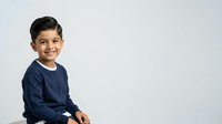 Young boy with dark hair and South Asian ethnicity, wearing navy blue long-sleeve shirt, smiling at camera against white background. Studio portrait suitable for family, education, and lifestyle designs.