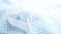 White satin ribbon shaped into a heart on soft blue fabric background, evoking romance, love, and tenderness for greeting cards.