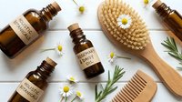 Natural organic skincare essentials with chamomile flowers, essential oil bottles, wooden brush and comb on white background for spa wellness routine.