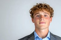 Young professional with curly blonde hair wearing gray suit jacket and blue checkered shirt smiling confidently against light background, copy space on right.