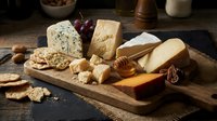Gourmet cheese board with assorted artisanal cheeses, crackers, nuts and honey on rustic wooden platter for entertaining and appetizer presentations.