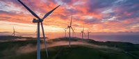 Wind turbines generating renewable energy on rolling hills at dramatic sunset with colorful sky and low clouds creating sustainable power landscape.