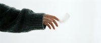 Hand in cozy green knit sweater holding a delicate white feather against a light background, evoking softness, freedom, and mindfulness.