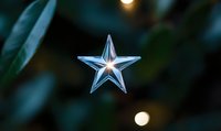 Luminous crystal star ornament with bokeh lights against dark green foliage background creates magical holiday atmosphere. Decorative element for festive designs.