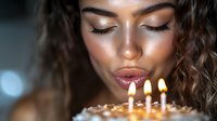 Young woman with curly hair making wish blowing out birthday candles on cake. Celebration moment with warm candlelight creating intimate atmosphere for special occasion.