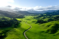 Winding dirt road through lush green rolling hills and valleys under dramatic cloudy sky. Rural countryside landscape with vibrant grass meadows and mountains.