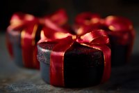 Dark chocolate truffles wrapped in elegant red satin ribbons on rustic surface, selective focus creates romantic mood for Valentine's Day or holiday gifting.