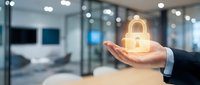 Businessman hand holding glowing padlock icon in modern office environment representing cybersecurity data protection and digital safety solutions.