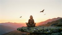 Peaceful blonde woman meditating on mountain cliff at sunrise with birds flying overhead, spiritual wellness and mindfulness concept for relaxation.