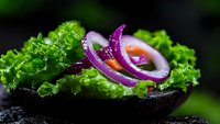 Fresh lettuce leaves and sliced purple onion rings arranged on dark surface with dramatic lighting, macro food photography for restaurant menu and culinary blogs.