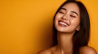Young Asian woman with bright genuine smile and closed eyes expressing joy and happiness against vibrant yellow background, radiating positive emotions.