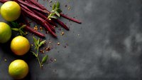 Fresh limes and red rhubarb stalks arranged on dark concrete background with scattered spices and mint leaves, moody food photography composition.