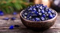 Raw lapis lazuli crystals in brown ceramic bowl on rustic wooden table, natural healing stones and minerals for crystal therapy and meditation.