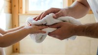 Caring hands gently drying with soft white towel in warm bathroom setting. Spa wellness treatment and personal hygiene concept for relaxation.