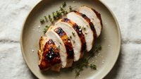 Sliced roasted duck breast with crispy skin on ceramic plate, garnished with fresh thyme sprigs, overhead food photography for culinary and restaurant use.