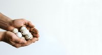 Man with dark skin tone holding white coconut balls in open palm against neutral background, suitable for food, nutrition, and wellness content.