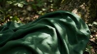 Close-up of crumpled dark green fabric draped on natural ground with scattered leaves and soil, showcasing texture and folds for design and lifestyle projects.