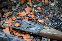 Charred wood and orange clay roof tile fragments scattered in ash and debris after fire damage, creating dramatic contrast of textures and colors.