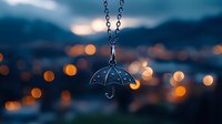 Silver umbrella pendant necklace against blurred city lights background with bokeh effect creates dreamy evening atmosphere, jewelry photography with shallow depth of field.