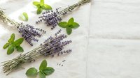 Fresh lavender bundles and mint leaves arranged on white linen fabric for natural aromatherapy and herbal wellness spa treatments.