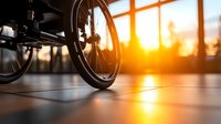 Close-up view of wheelchair wheel at sunset with warm golden light streaming through window, creating silhouette against tiled floor, representing mobility and hope.