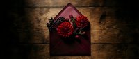 Burgundy envelope with dark red chrysanthemum flowers on rustic wooden background for romantic correspondence and wedding invitations.