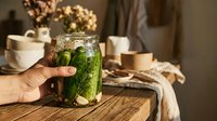 Refreshing cucumber water infused with fresh mint leaves in a clear glass held by hand on wooden table with blurred home interior background for beverage and wellness content.
