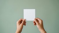 Female hands holding blank white card against soft sage green background for mockup and branding purposes.