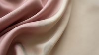 Soft pink and beige silk fabric with elegant flowing folds and gentle curves creating luxurious textile background for fashion and interior design projects.