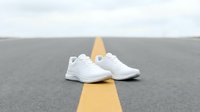 Pair of white athletic sneakers positioned on asphalt road with yellow center line, isolated on gray background for design and commercial use.