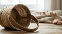 Woven wicker basket tipped over spilling autumn leaves on rustic wooden table in cozy home interior setting for seasonal decor and harvest themes.