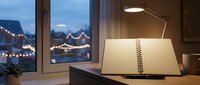 Cozy evening workspace with open notebook and desk lamp by window overlooking festive Christmas market lights creating warm productive atmosphere for writing.