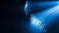 Blue fiber optic cables with glowing light particles streaming through dark background for technology and communication concepts.