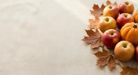 Fresh autumn apples and small pumpkins with dried maple leaves arranged on neutral background for seasonal harvest decorating and thanksgiving concepts.