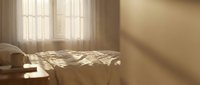 Warm sunlight streaming through bedroom window creating geometric shadows on unmade bed with soft linens in cozy morning interior space for relaxation concepts.