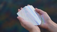 Young adult hands holding iridescent soap bubble with rainbow light reflections, isolated against blurred background for design and creative projects.