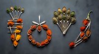Creative food art spelling JOY with colorful spices, herbs and vegetables arranged on dark slate background for festive holiday cooking and kitchen decor.