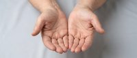 Male hands cupped together in giving gesture on white background, open palms facing up showing generosity and offering support for charity concepts.
