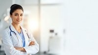 Confident female doctor with stethoscope standing with crossed arms in modern hospital setting, professional healthcare worker ready for patient care.