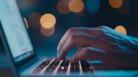 Close-up of hands typing on laptop keyboard at night with glowing bokeh lights in background, creating atmospheric digital workspace mood.