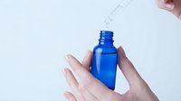 Woman applying blue serum from dropper bottle onto palm for skincare routine and beauty treatment on white background.