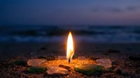 Glowing candle flame on sandy beach at twilight with ocean waves in background creating peaceful meditation atmosphere for relaxation and mindfulness.