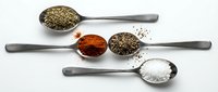 Assorted colorful spices and seasonings in metal measuring spoons arranged on white background for culinary cooking and food preparation.