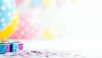 Colorful birthday party setup with gift boxes and confetti on white table against pastel balloon background for celebration events and festive occasions.