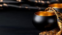 Elegant black ceramic cup with golden interior on dark background with luxurious golden fabric, dramatic lighting creates mysterious oriental atmosphere.