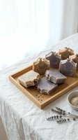 Handmade artisan soap bars with lavender decoration arranged on wooden tray over white linen fabric for natural skincare and spa wellness routine.
