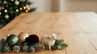 Festive holiday ornaments and evergreen garland arranged on wooden table with blurred decorated tree in background, perfect for seasonal marketing and holiday design projects.